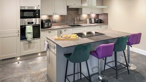 Una cocina moderna con una isla central, taburetes de bar, electrodomésticos de acero inoxidable y un amplio ventanal.