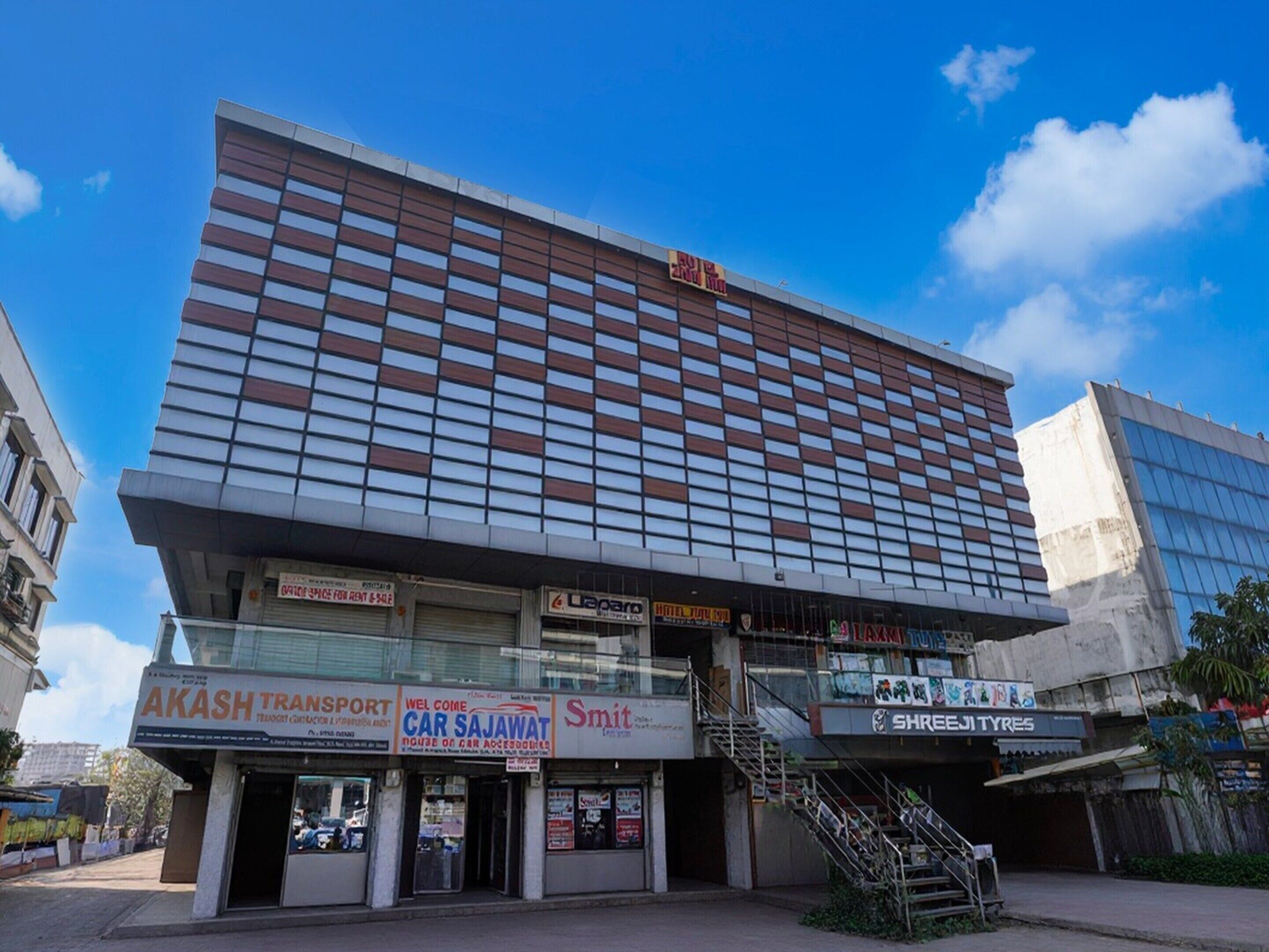 Un immeuble à plusieurs étages abritant divers commerces au rez-de-chaussée, notamment une entreprise de transport, un magasin d’accessoires automobiles et un hôtel.