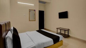 A hotel room with a bed, a bedside table, a mirror, and a TV on the wall. - Hotel O Vapi Gidc Formerly Zion Inn (Vapi)