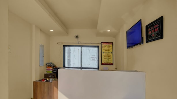 A reception area with a wooden reception desk, a blue television, and a digital clock on the wall. - Hotel O Vapi Gidc Formerly Zion Inn (Vapi)