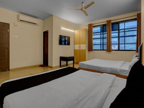 A hotel room with two beds, a desk, a television, and a window with curtains.
