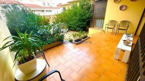 Une petite terrasse avec une table et des chaises, entourée de plantes en pot et dotée d’un sol carrelé.