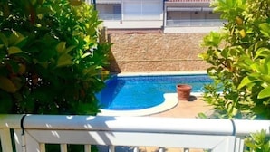 En swimmingpool omgivet af grøn vegetation, med en stenvæg og en bygning i baggrunden.