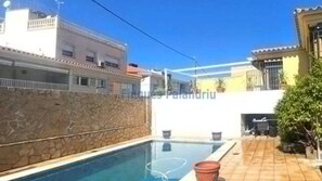 Une piscine avec un mur en pierre d’un côté et une terrasse carrelée avec des meubles d’extérieur.