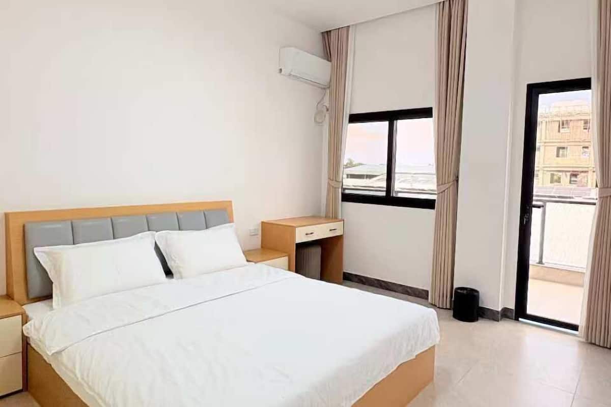 A hotel room with a bed, nightstands, a window with curtains, and a view of buildings outside.
