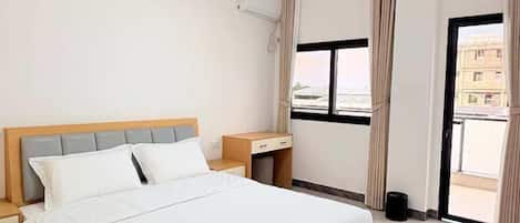 Una habitación de hotel con cama, mesitas de noche, una ventana con cortinas y vistas a edificios.