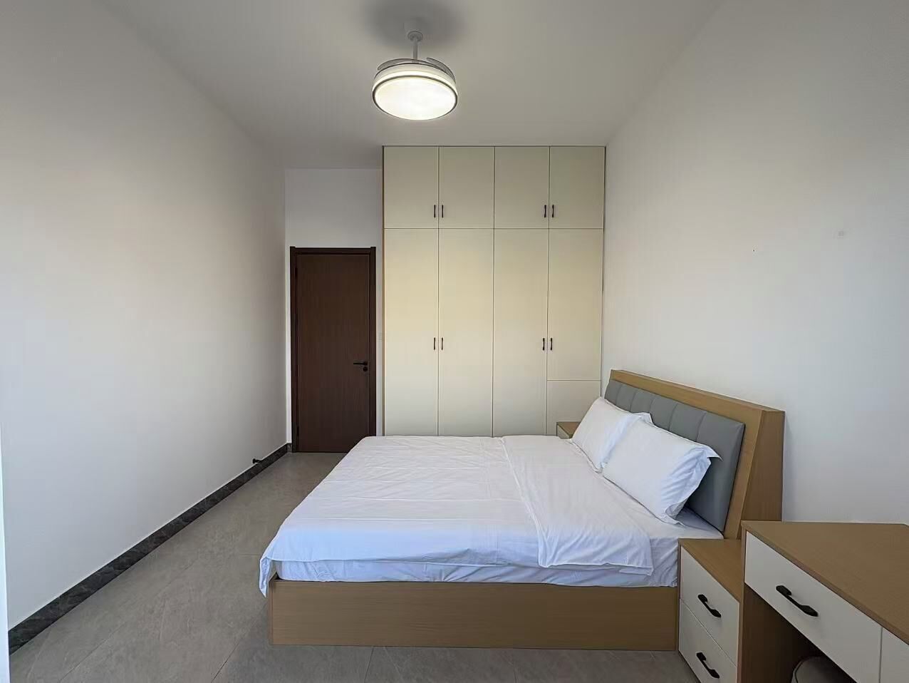 A bedroom with a bed, a wardrobe, a bedside table, and a door.