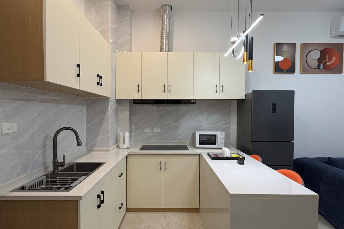 A modern kitchen with white cabinets, a built-in microwave, a black refrigerator, and a dining area with a blue sofa.