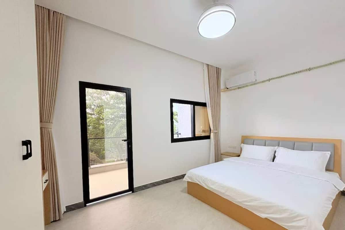 A bedroom with a bed, a window, a door, and a ceiling light.