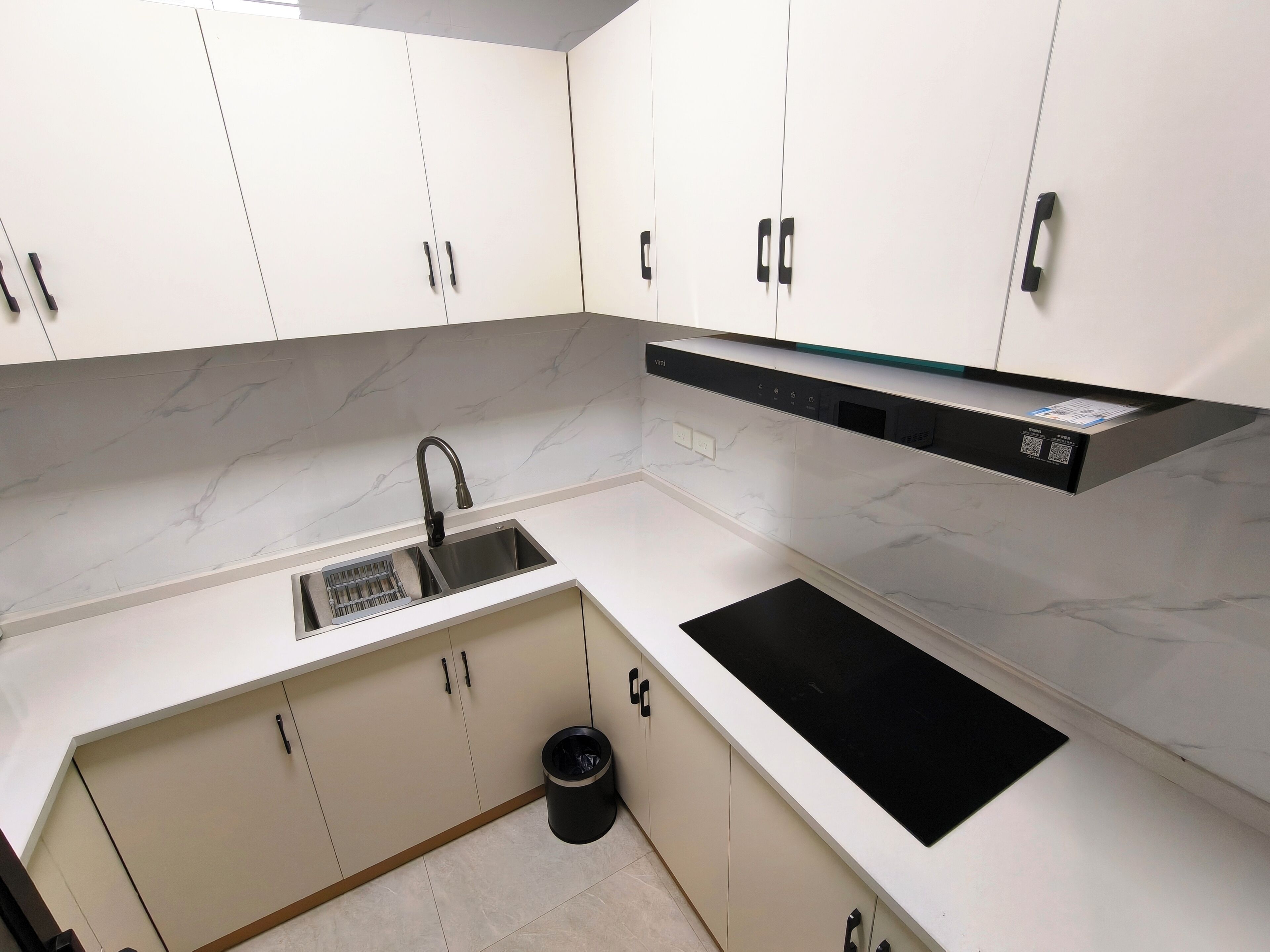 Una cocina moderna con gabinetes blancos, un lavamanos de acero inoxidable, una encimera negra y una estufa negra.