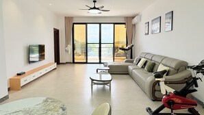 Un salon moderne avec un canapé, un téléviseur, un vélo d’exercice et un balcon offrant une vue agréable.