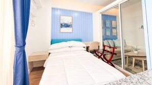 A modern bedroom with a bed, a desk, and a chair. There is a sliding glass door leading to a balcony with seating. - Maree- Verdon Parc, Davao City (Davao City)