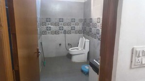 A bathroom with a toilet, a blue step stool, and a shower area. - Hotel Yamuna Palace (Gurugram)