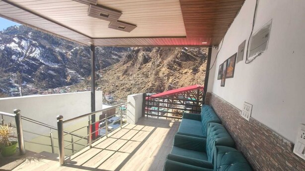 A balcony with a view of snow-covered mountains, a wooden ceiling, and a green cushioned seating area. - Hotel Yamuna Palace (Gurugram)