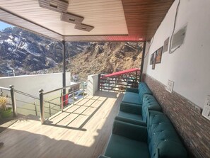 Un balcón con vistas a montañas nevadas, techo de madera y zona de estar con cojines verdes.