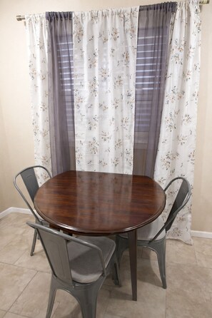 Un coin repas avec une table ronde en bois et quatre chaises en métal.