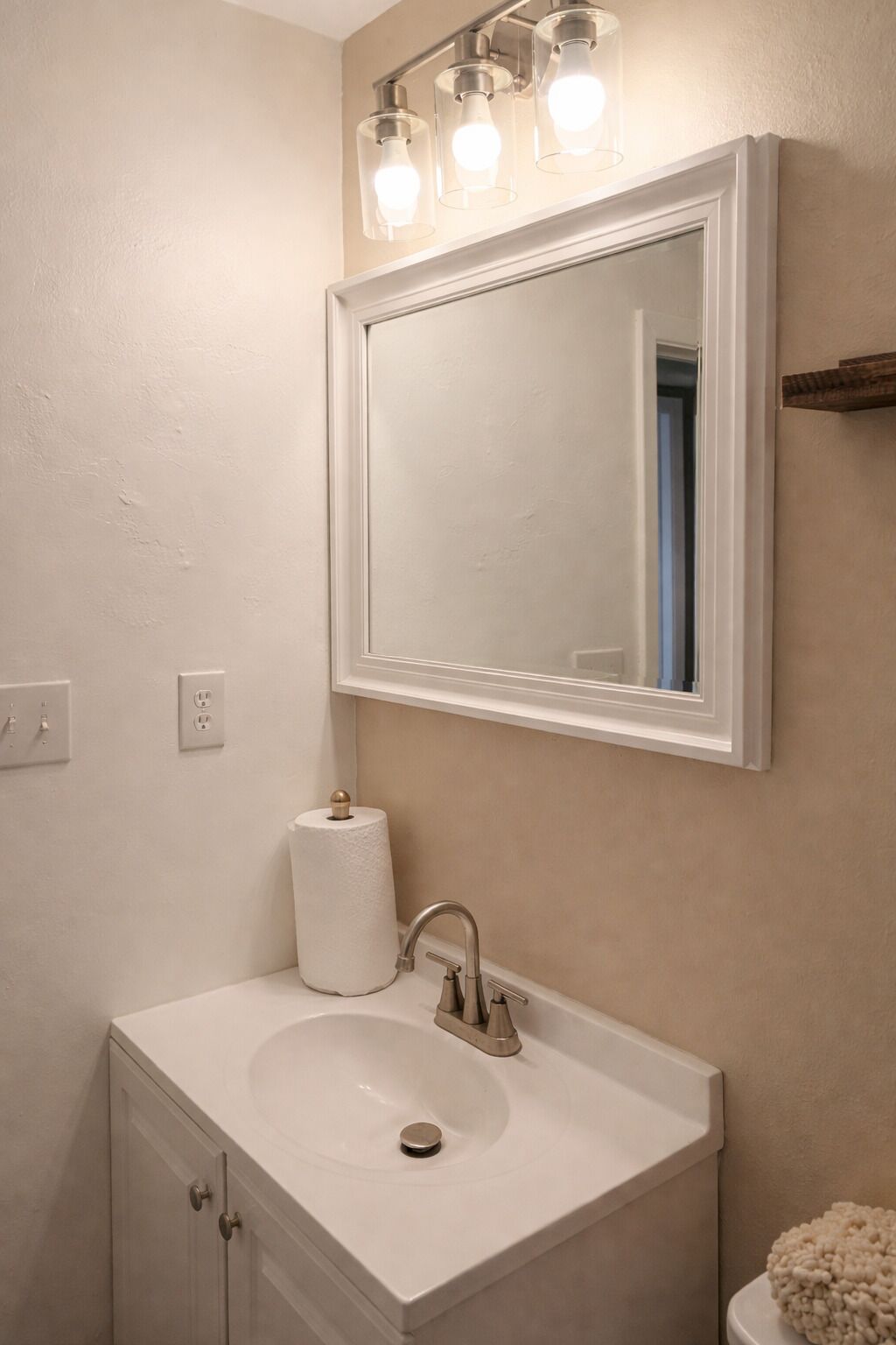 A bathroom with a white sink, a mirror, and a towel dispenser.