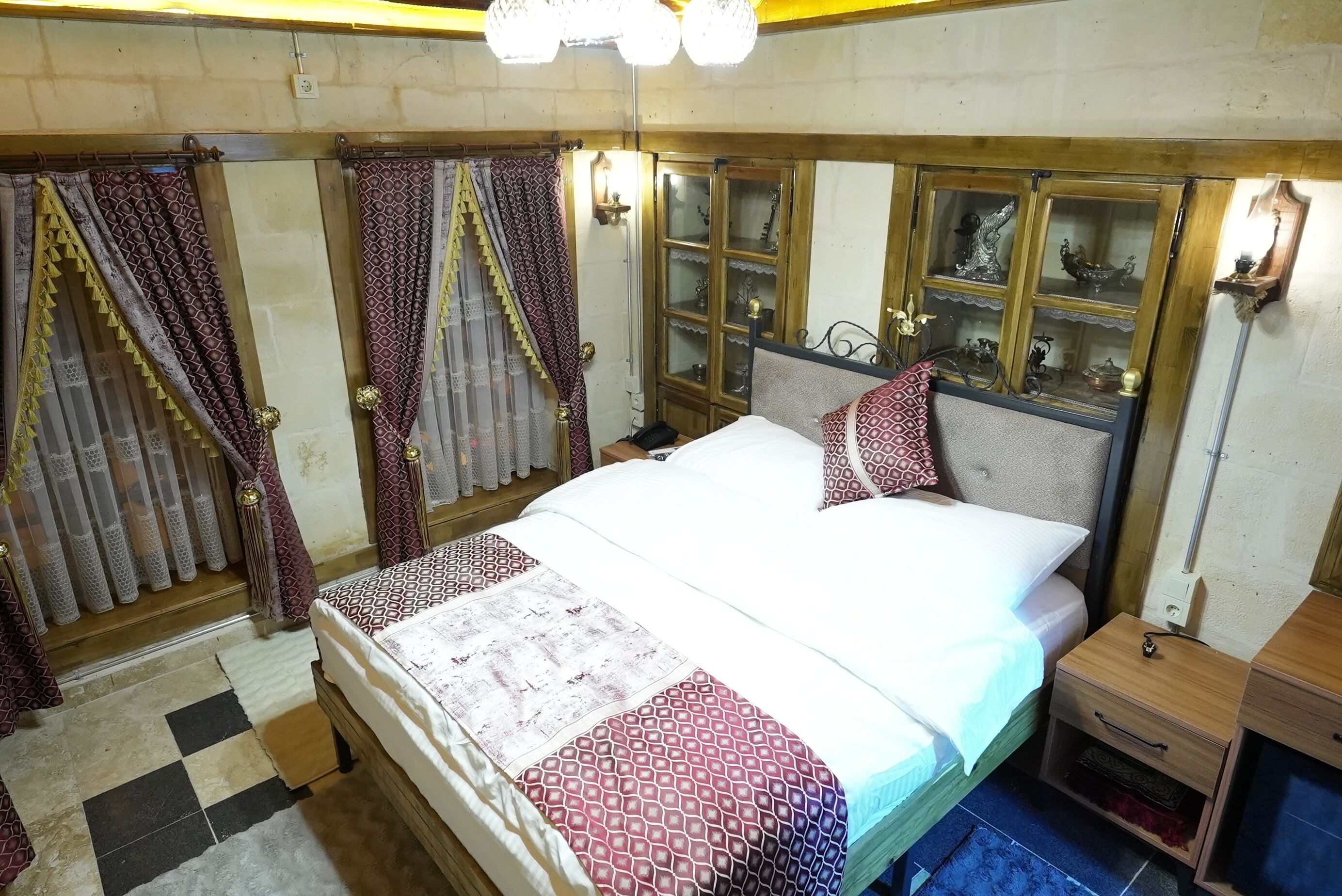 A room with a bed, curtains, a nightstand, a mirror, and a cabinet with glass doors.