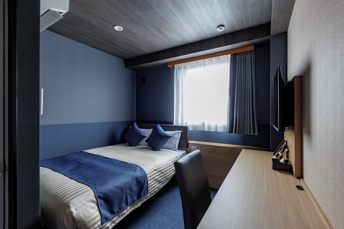 Una habitación pequeña con cama, escritorio y ventana con cortinas.