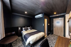 Habitación de hotel con cama, escritorio, silla, aire acondicionado y puerta.
