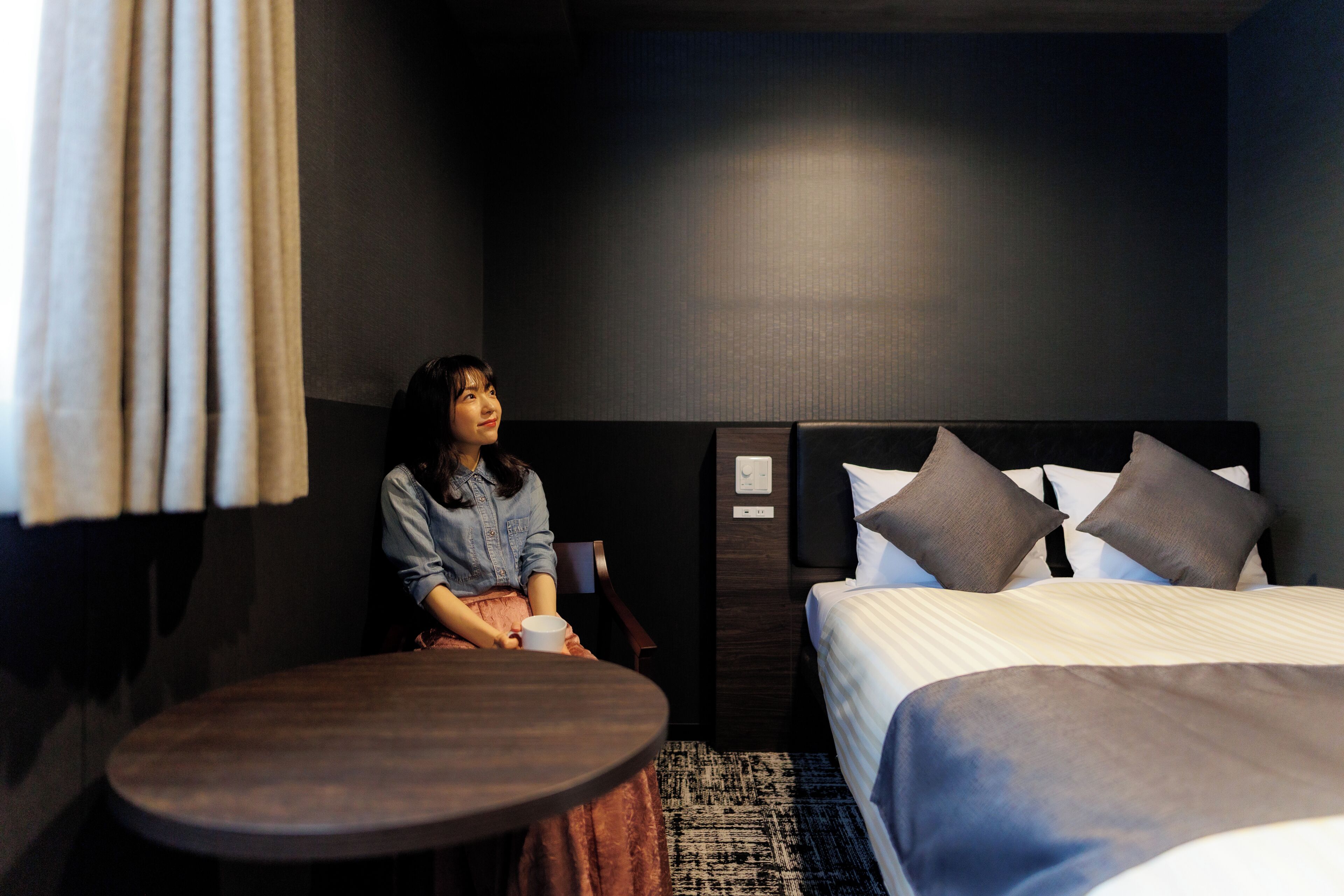 A hotel room with a bed, a round table, and a person sitting at the table.