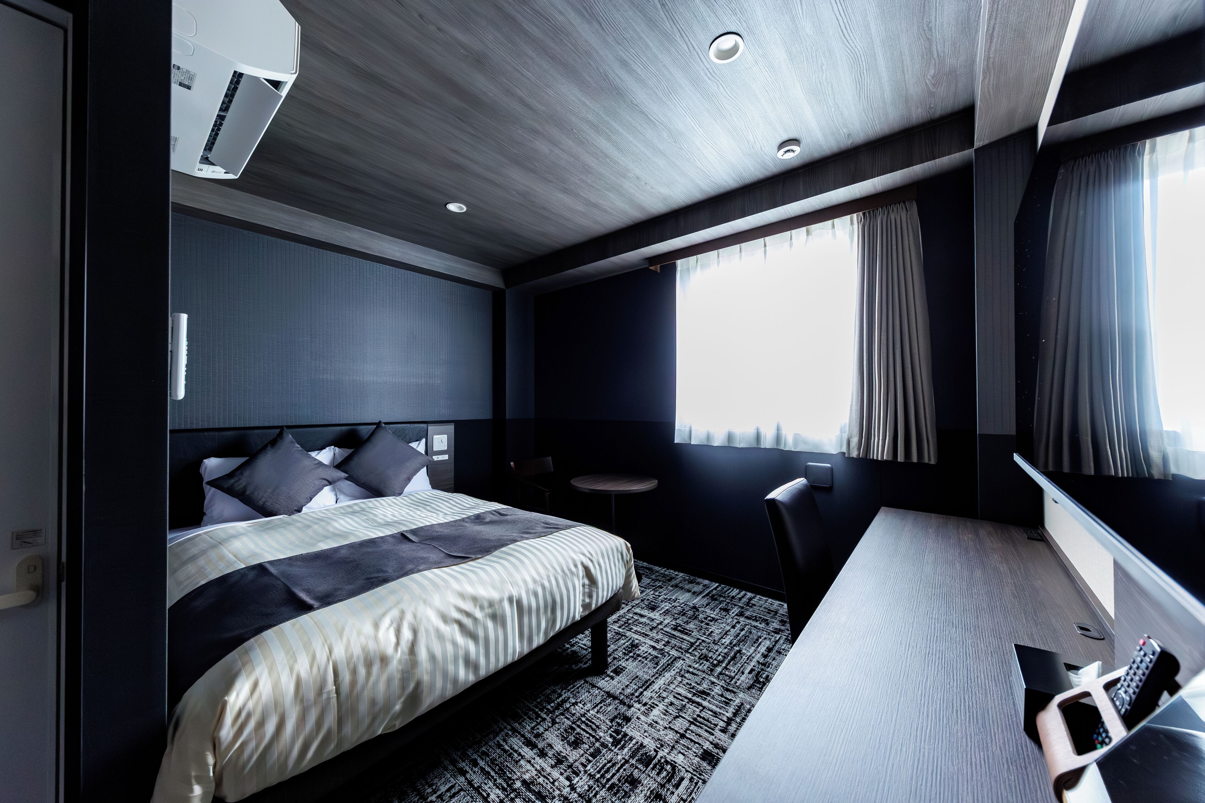 Una habitación de hotel moderna con cama, escritorio, silla, una mesita y ventana con cortinas.