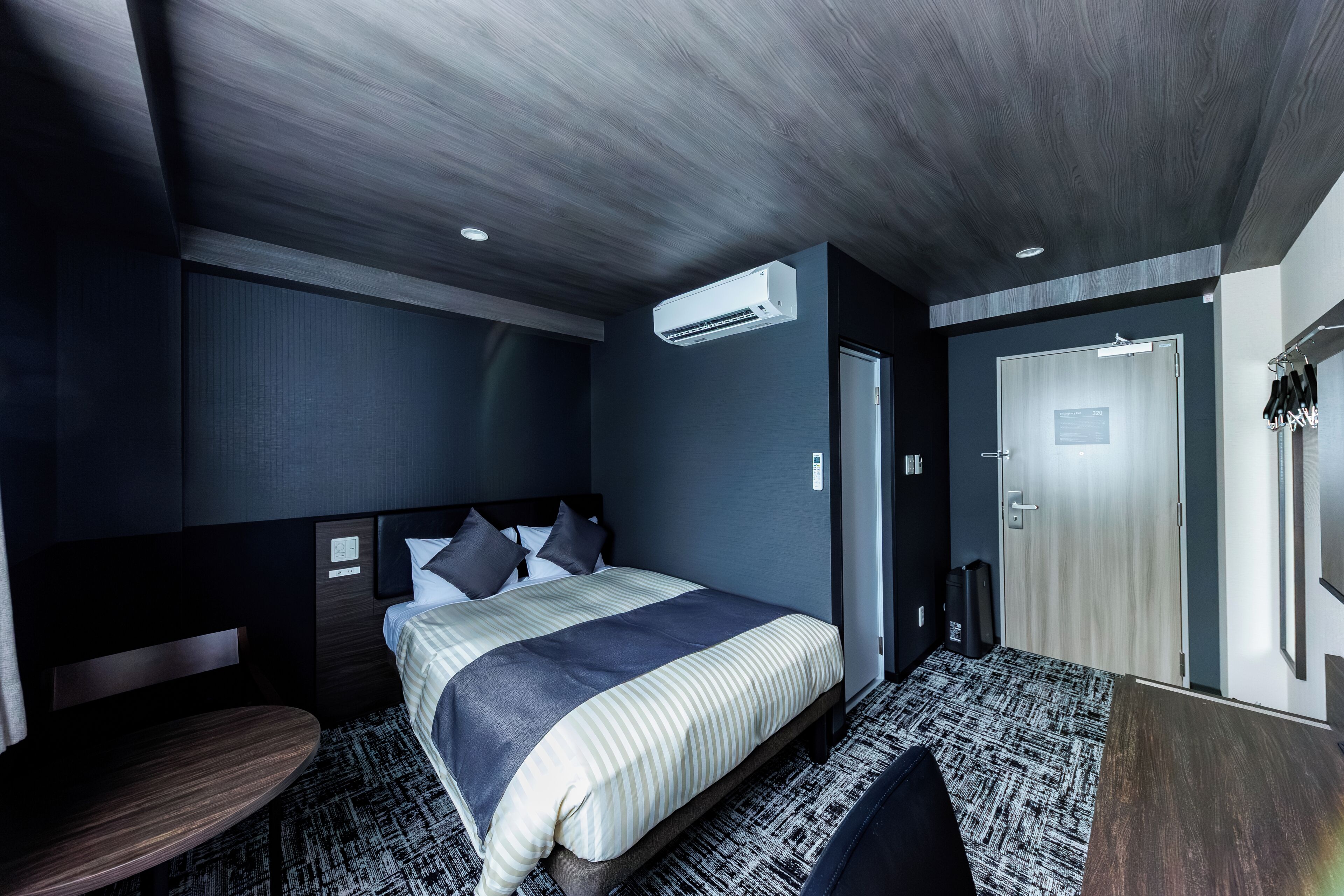 Ein modernes Hotelzimmer mit einem Bett, einem Nachttisch und einer Tür zu einem Badezimmer.