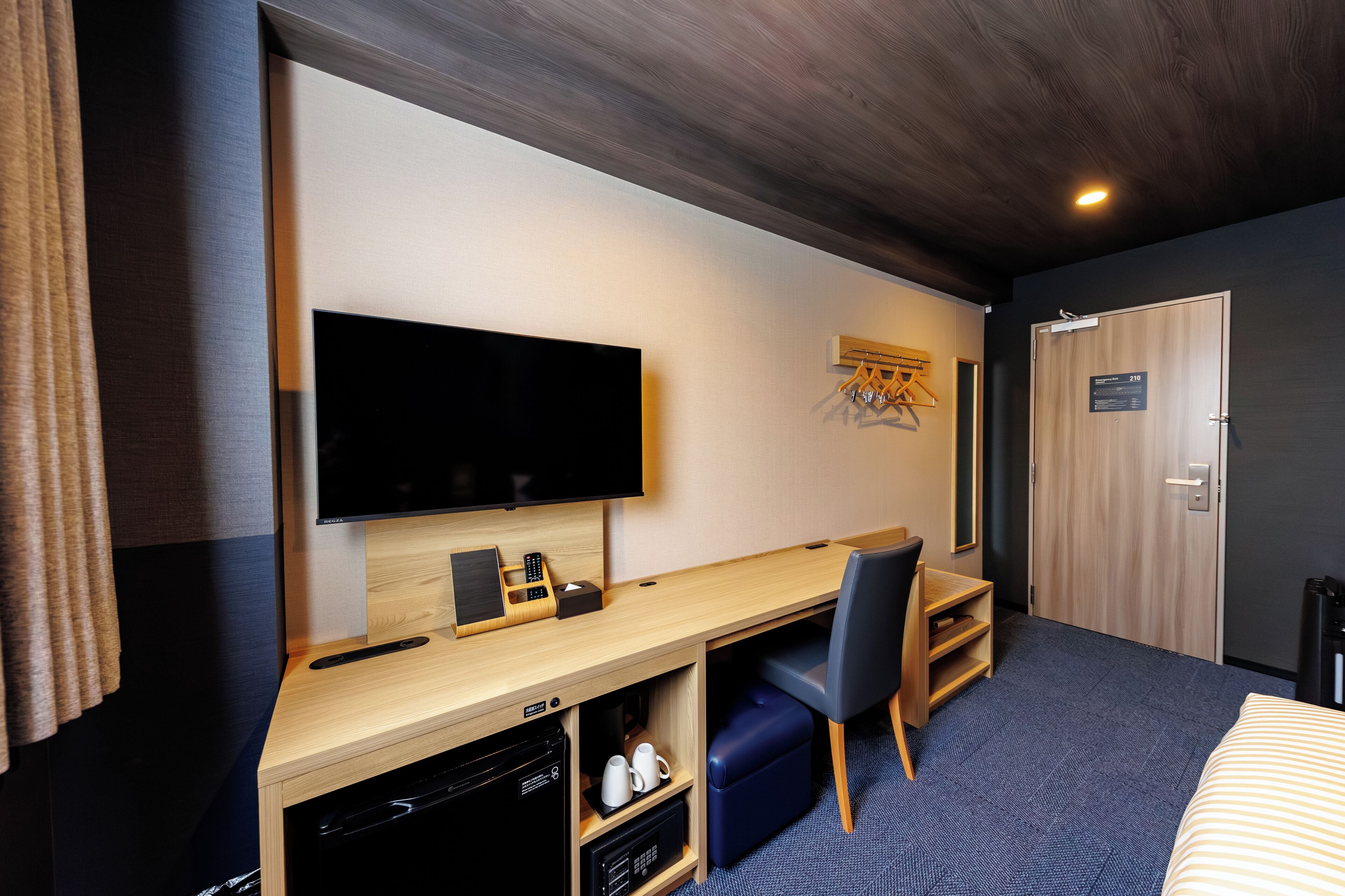 A hotel room with a flat-screen TV, wooden desk, blue chair, and a bed with striped bedding.