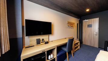 A hotel room with a flat-screen TV, wooden desk, blue chair, and a bed with striped bedding.