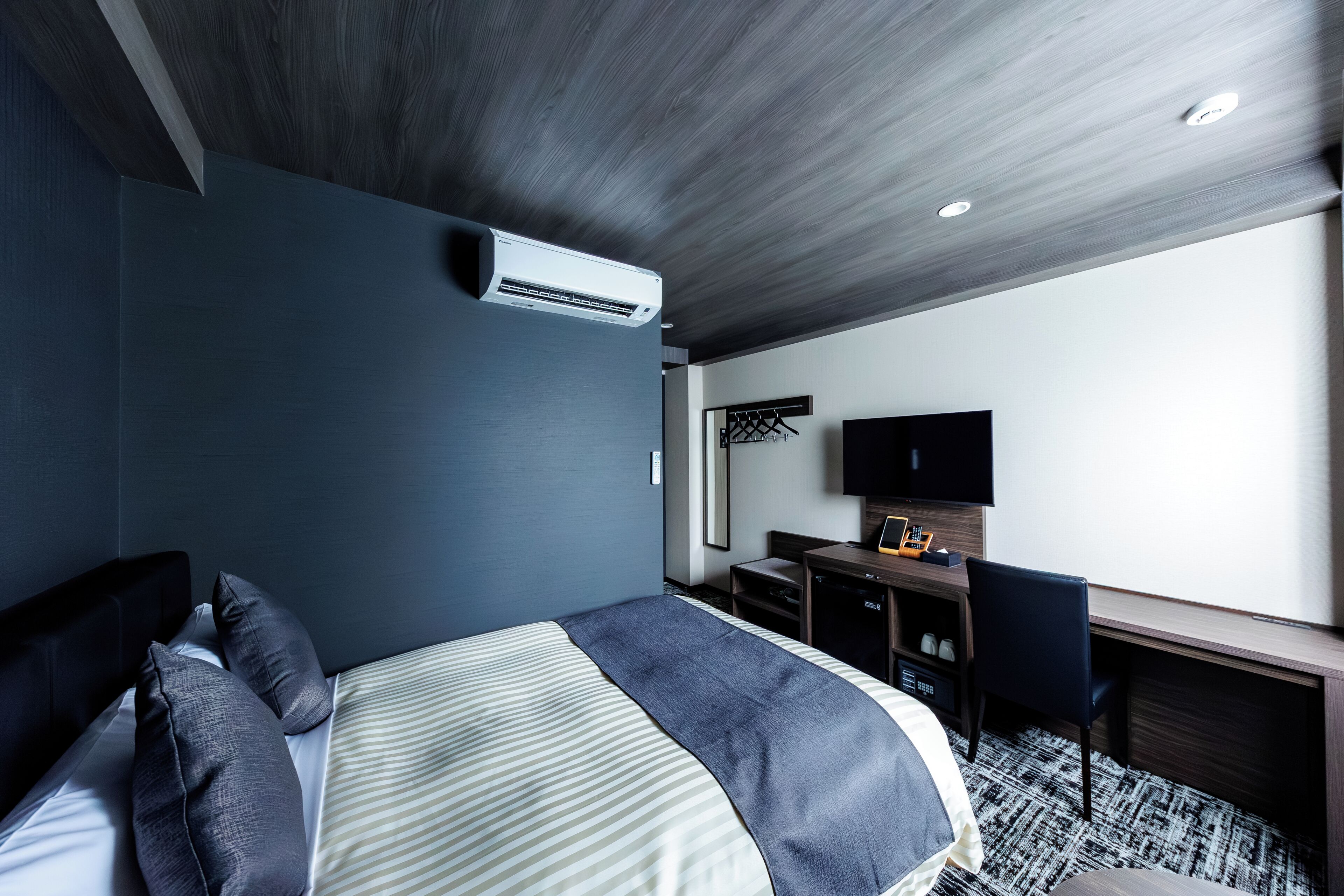 Habitación de hotel con cama, escritorio, silla, televisión de pantalla plana y aire acondicionado.