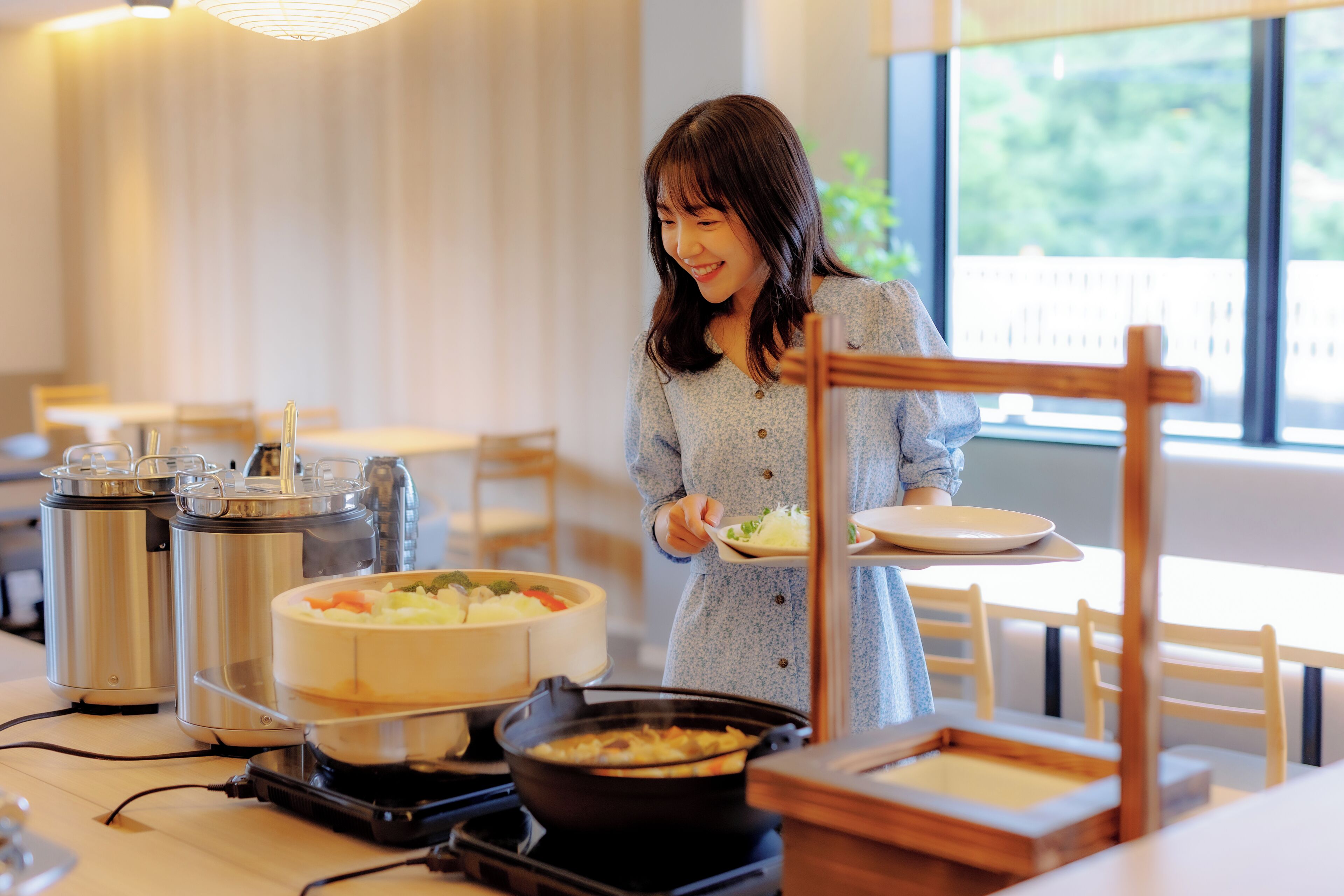 A person serving food in a modern dining area with a view of greenery outside.