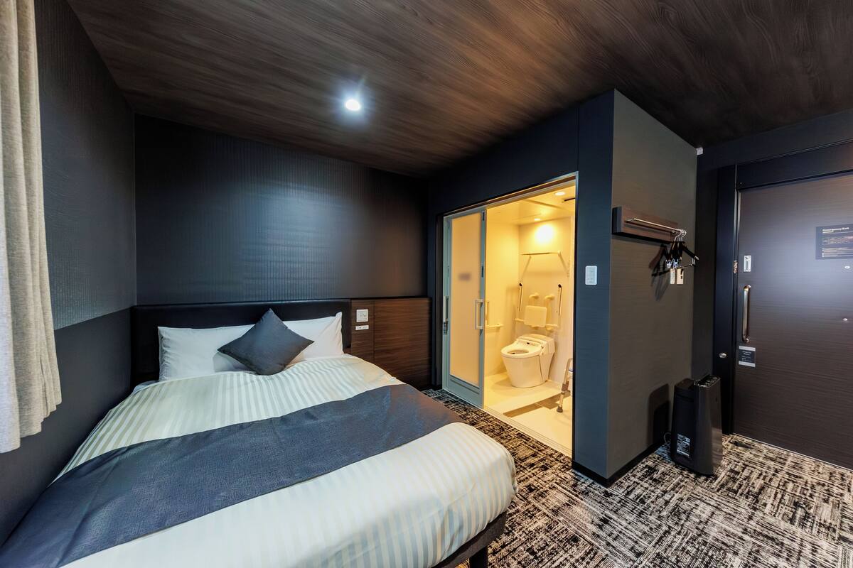 Habitación de hotel con cama, puerta que da a un baño y un altavoz negro pequeño.