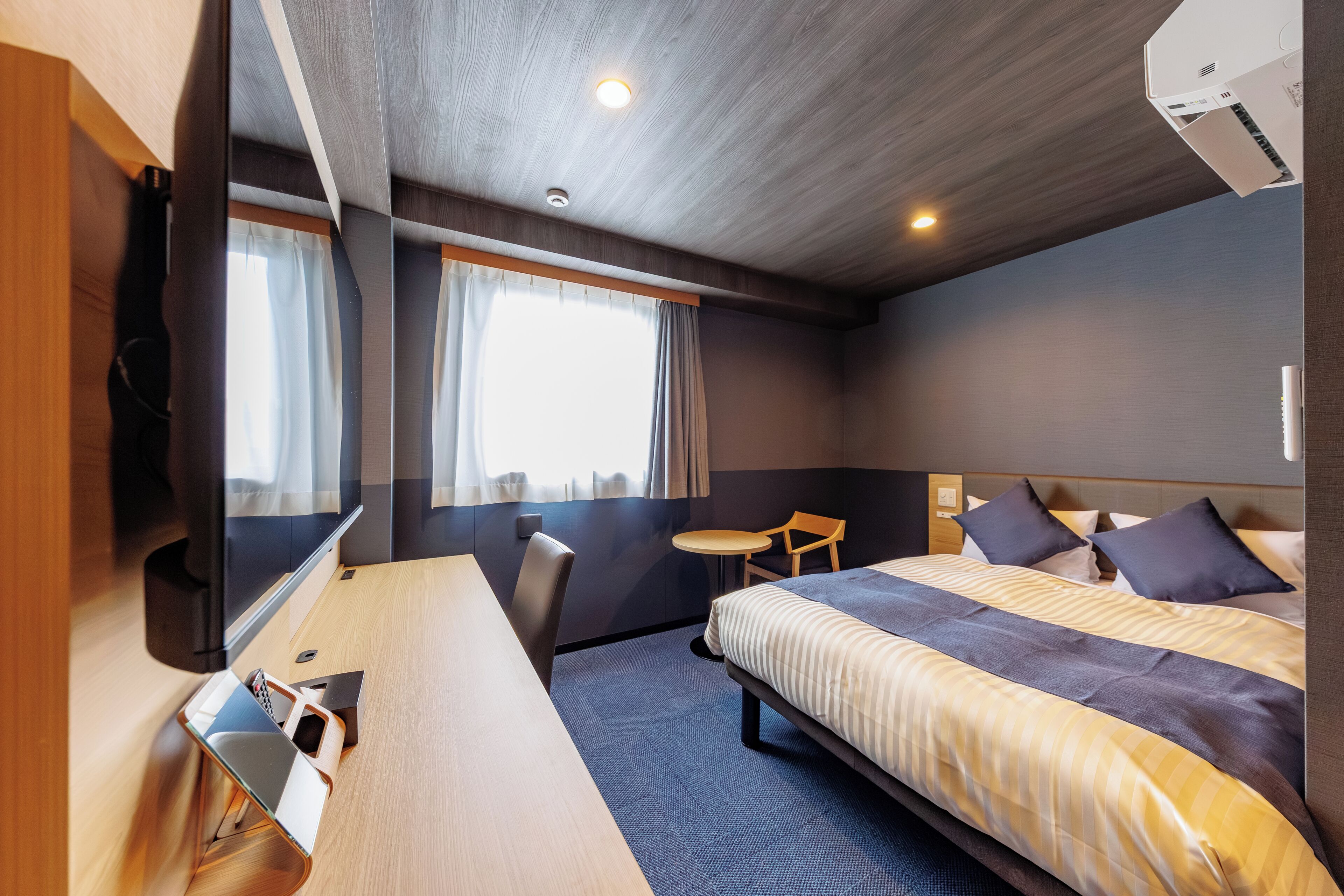 Una habitación de hotel con cama, escritorio, silla, mesita y televisión.