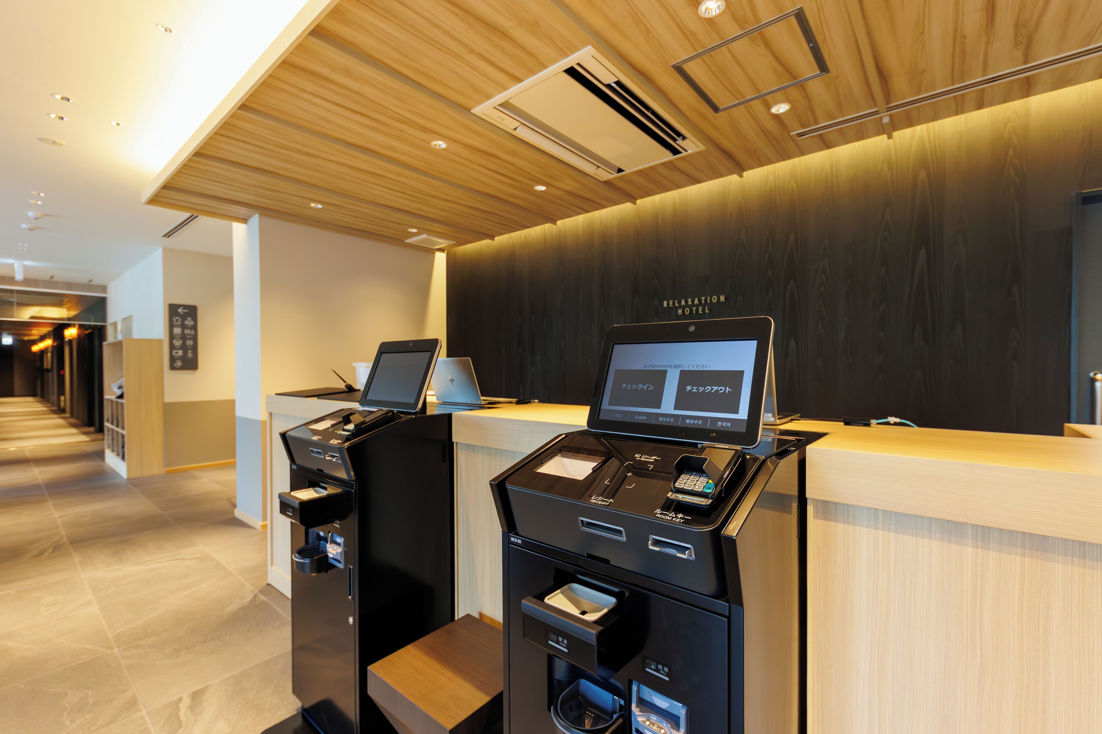 A reception desk with a digital screen, a cash register, and a self-service kiosk in a hotel lobby.