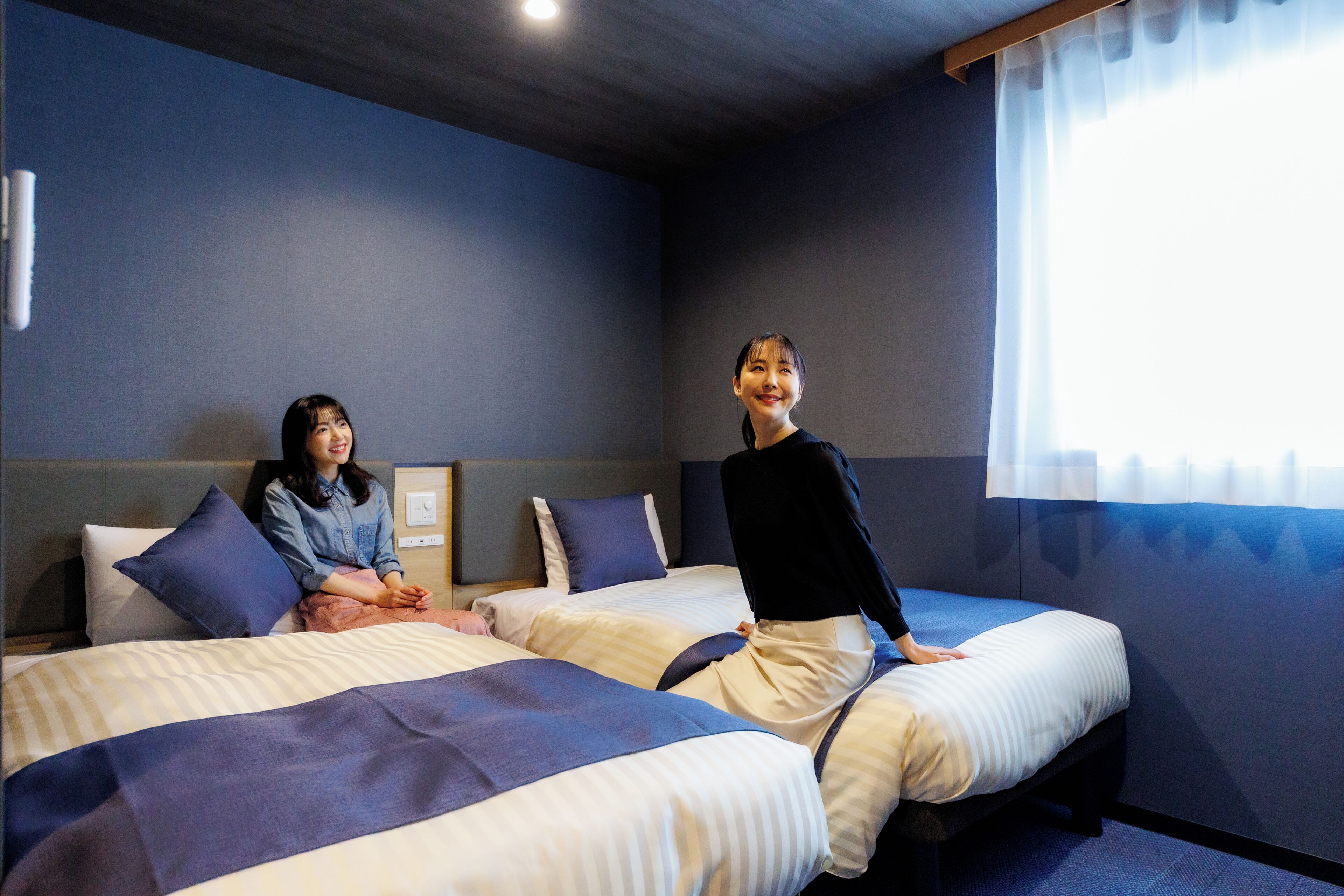 A hotel room with two beds, a window with curtains, and a headboard.