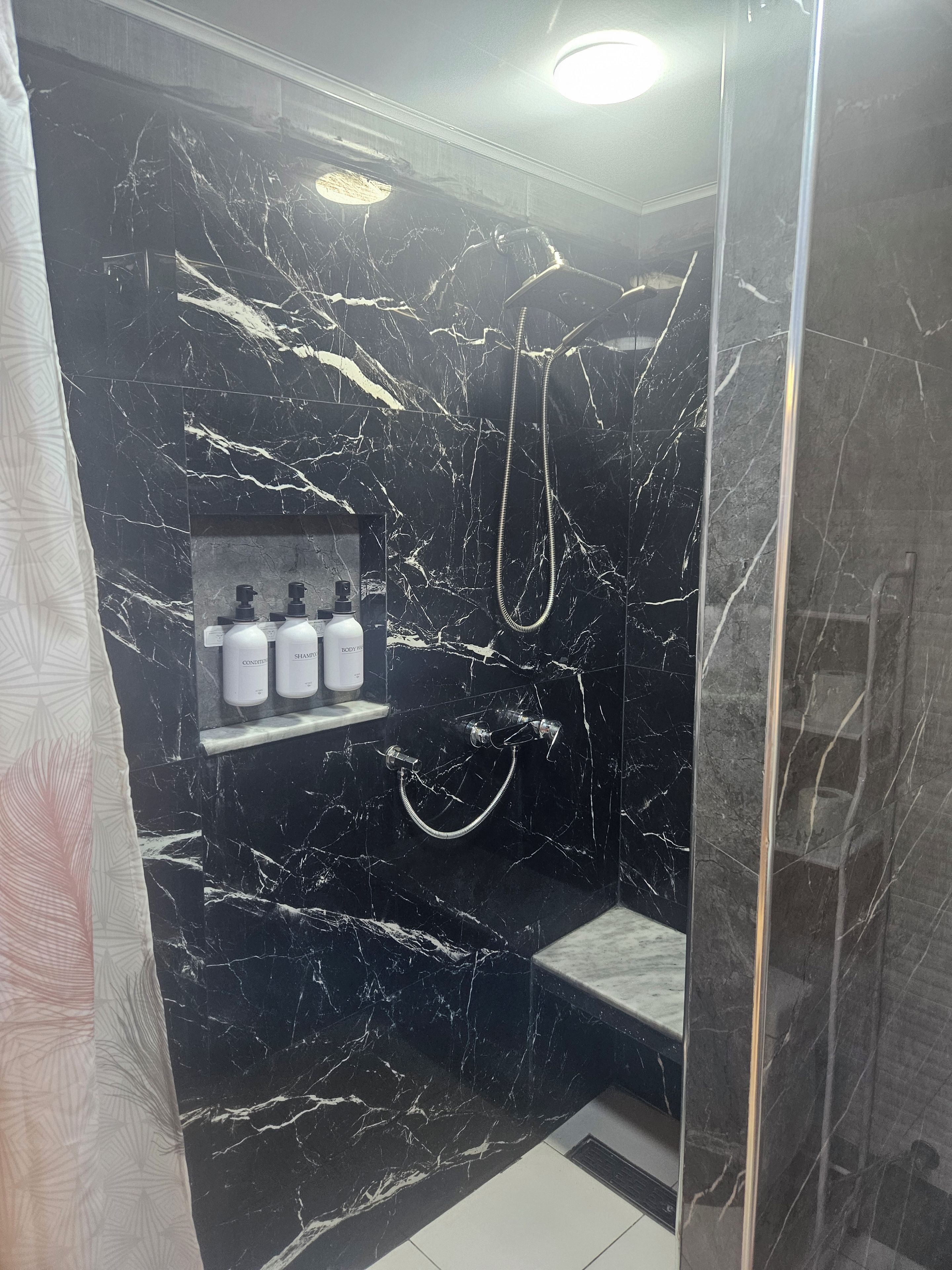 Ein Badezimmer mit schwarzem Marmor, einer Dusche inklusive Handbrause und einem Ablagebereich für Toilettenartikel.