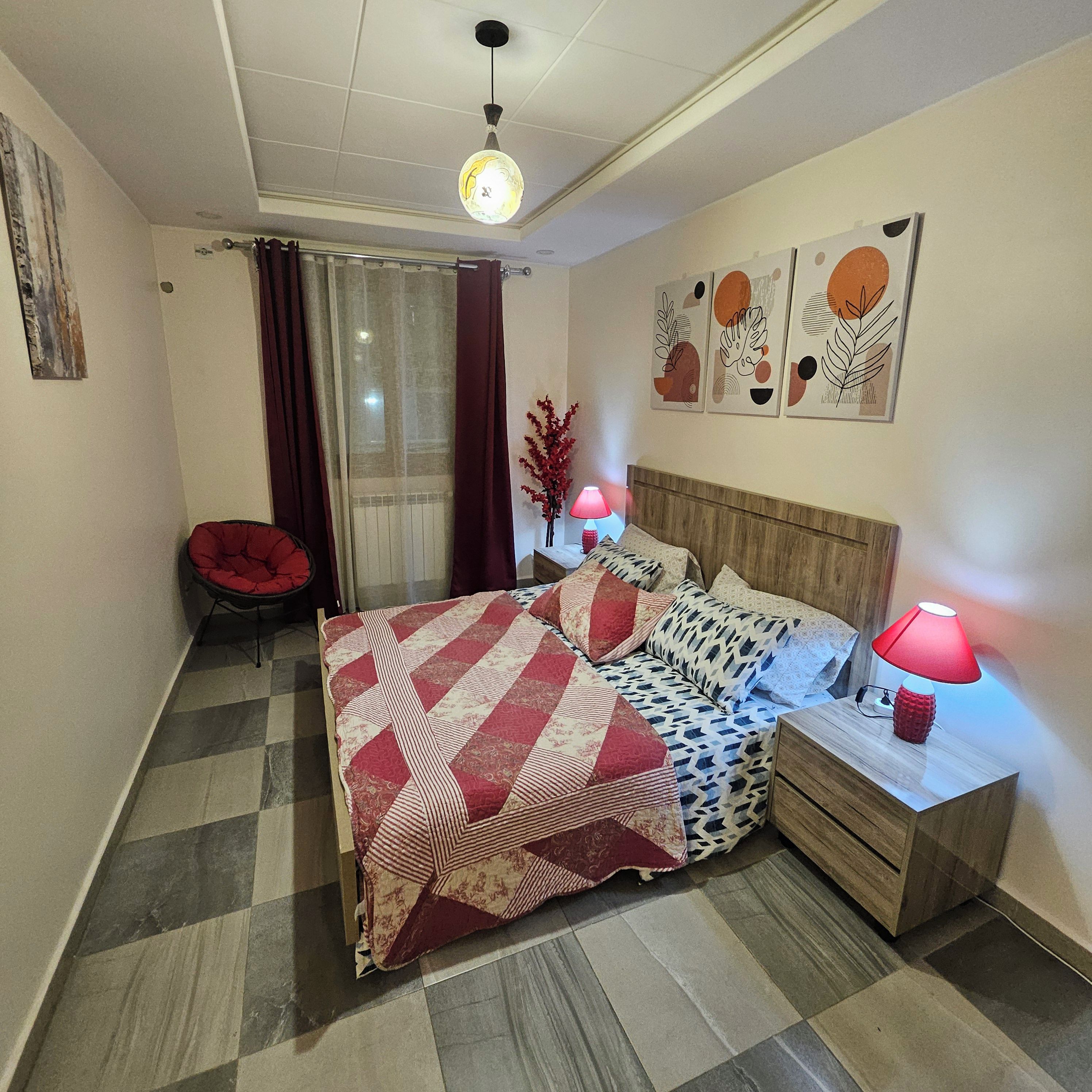 A bedroom with a bed, a nightstand, a lamp, a chair, and artwork on the wall.
