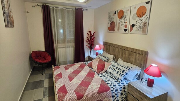 Et soveværelse med seng, et natbord, en lampe, en stol og kunst på væggen.