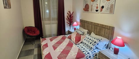 A bedroom with a bed, a nightstand, a lamp, a chair, and artwork on the wall.