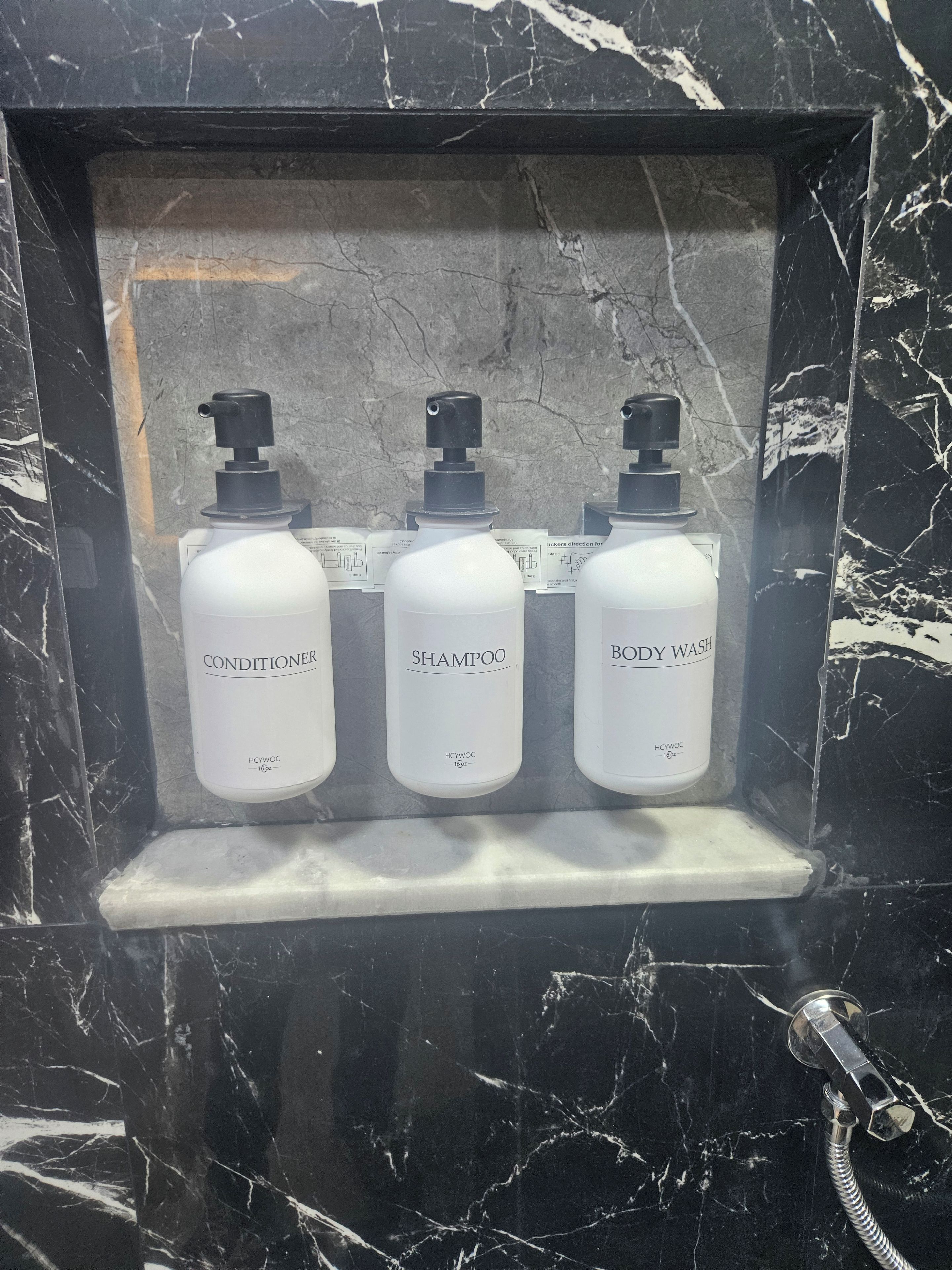 Een marmeren lijst rond een plank met drie witte flessen, gelabeld als conditioner, shampoo en douchegel.