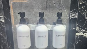 En reol med marmorgulv, hvori der står tre hvide flasker mærket balsam, shampoo og kropsvask.