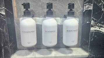 Een marmeren lijst rond een plank met drie witte flessen, gelabeld als conditioner, shampoo en douchegel.