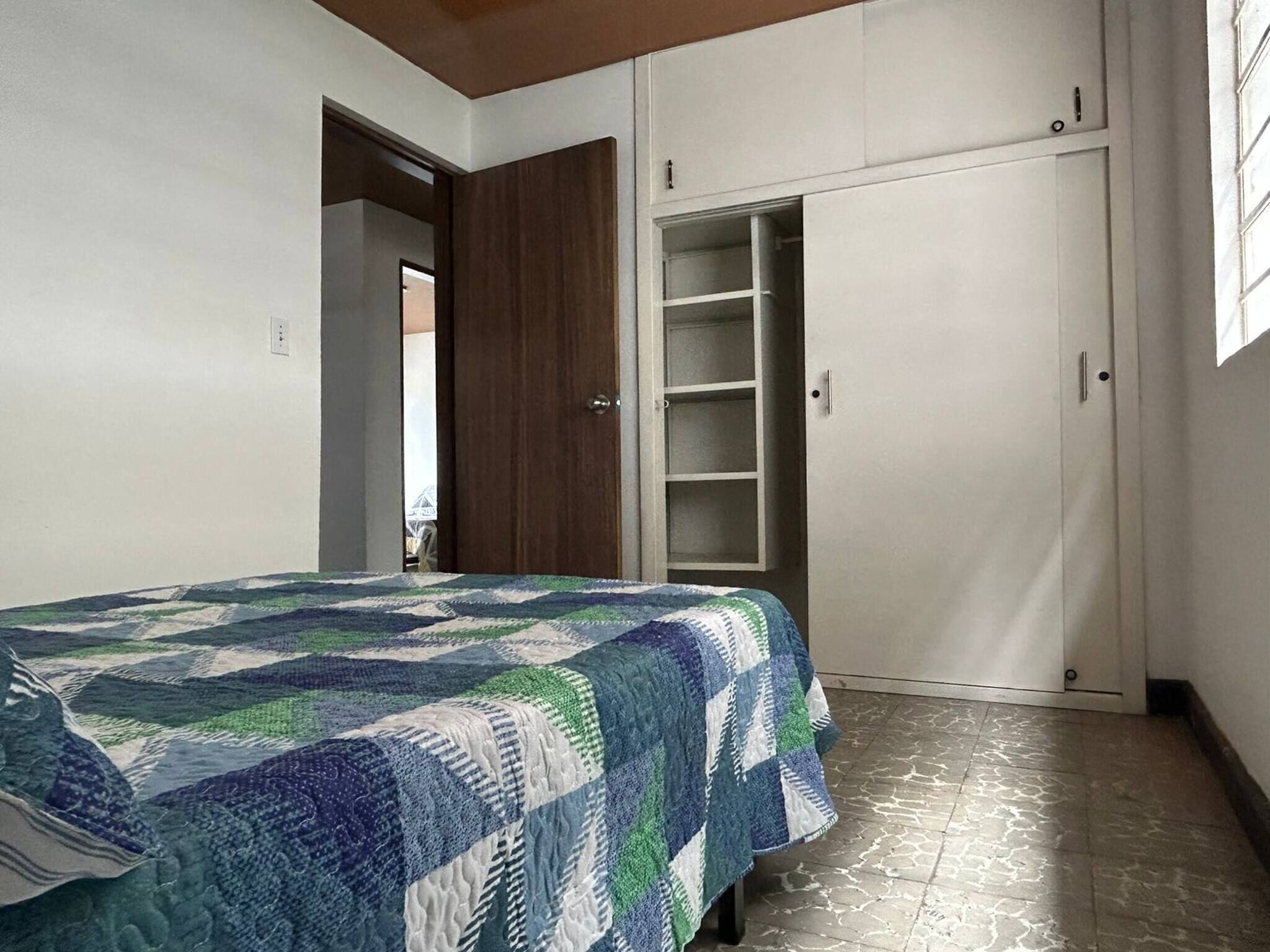 A bedroom with a bed, a wardrobe, and a door leading to another room.