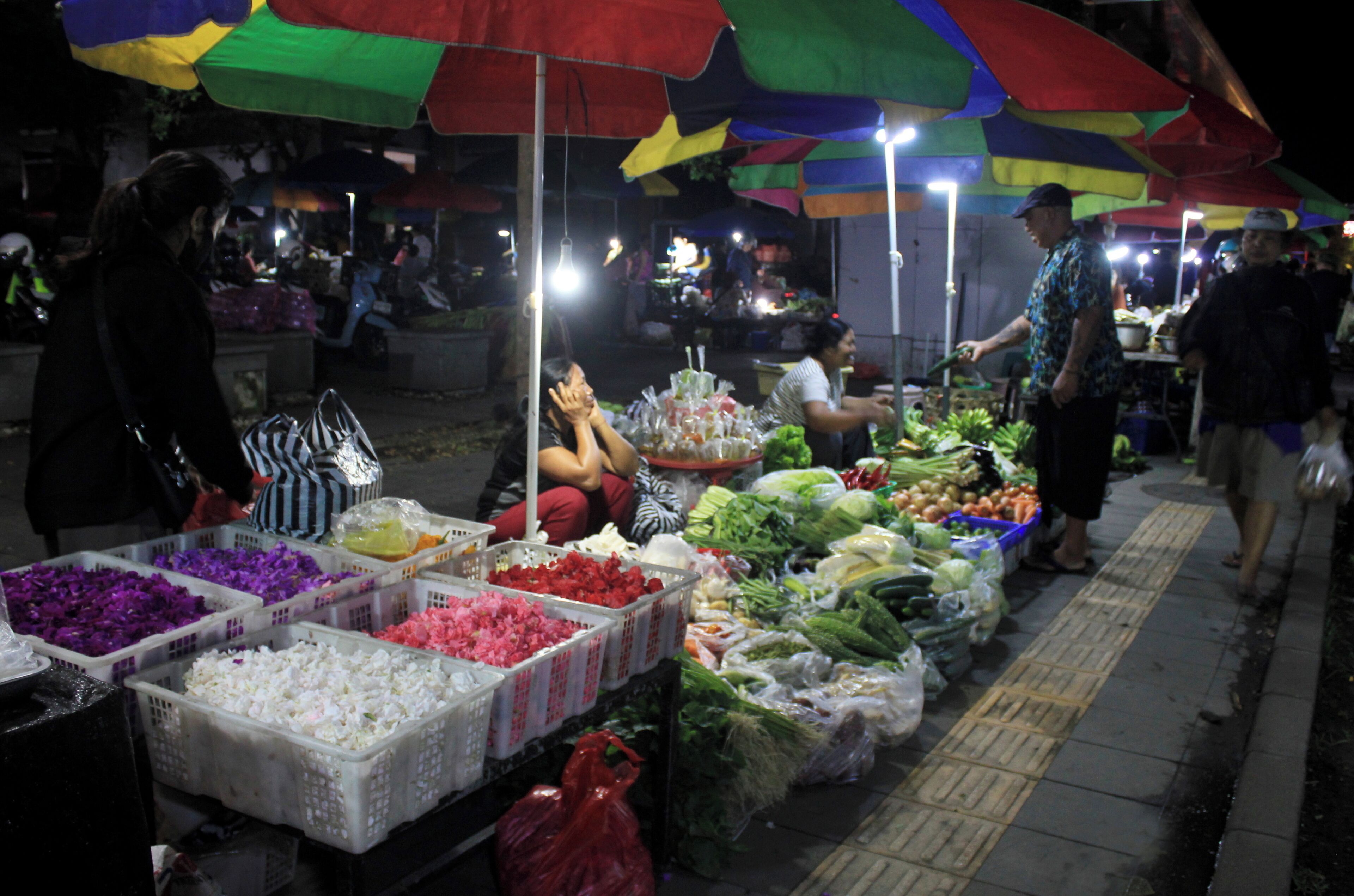Een nachtelijke markt in de open lucht met verschillende kraampjes die verse producten verkopen onder kleurrijke parasols.