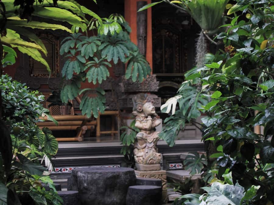 Un jardín tradicional con estatuas de piedra, plantas frondosas y un banco de madera.