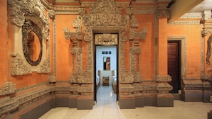 An ornate hallway with intricate carvings, a mirror, and a door at the end. - Tusantha Ubud A Trishula Collection (Ubud)