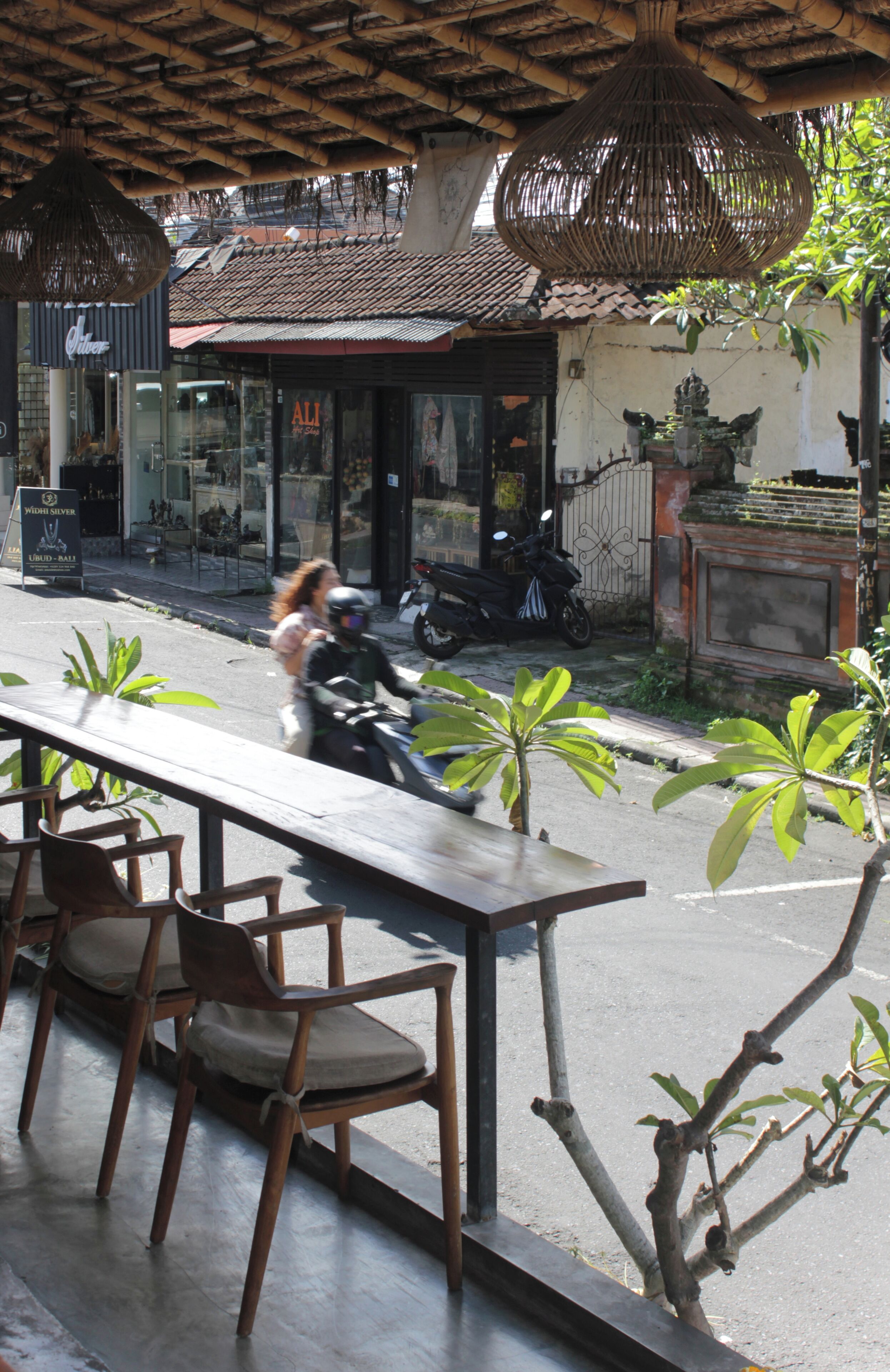 Straßenansicht mit einem Restaurant, Außenbereich und einem vorbeifahrenden Motorrad.