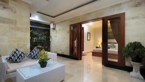 A modern living room with a sofa, a coffee table, and a potted plant. There is a door leading to another room. - Tusantha Ubud A Trishula Collection (Ubud)