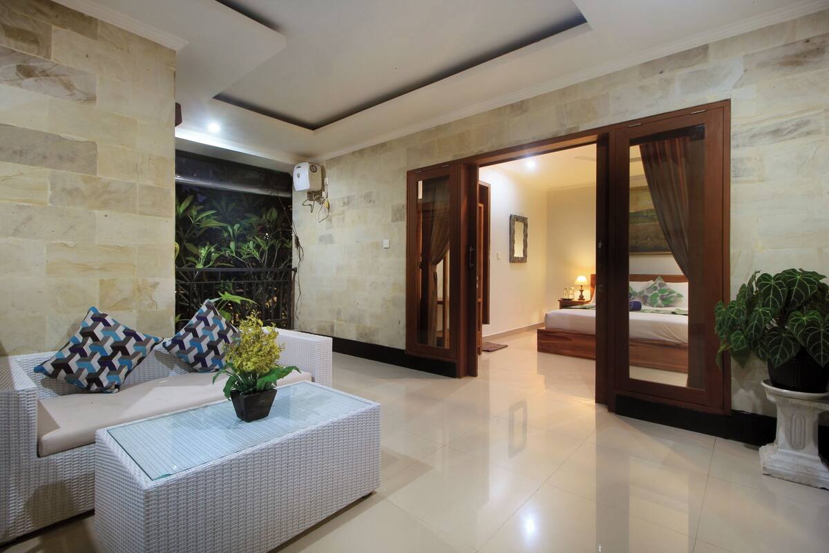 Una sala de estar moderna con un sofá, una mesa de centro y una planta en maceta. Hay una puerta que da a otra habitación.