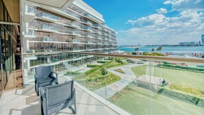 A modern hotel with a glass facade, outdoor seating, and a view of the coastline. - PVH - The8 - Opulent 3BR - Beach Access (Dubai)